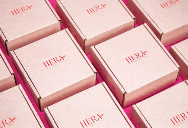 Campaign photography for Hera Organics showing branded product packaging arranged in a geometric pattern on a pink background
